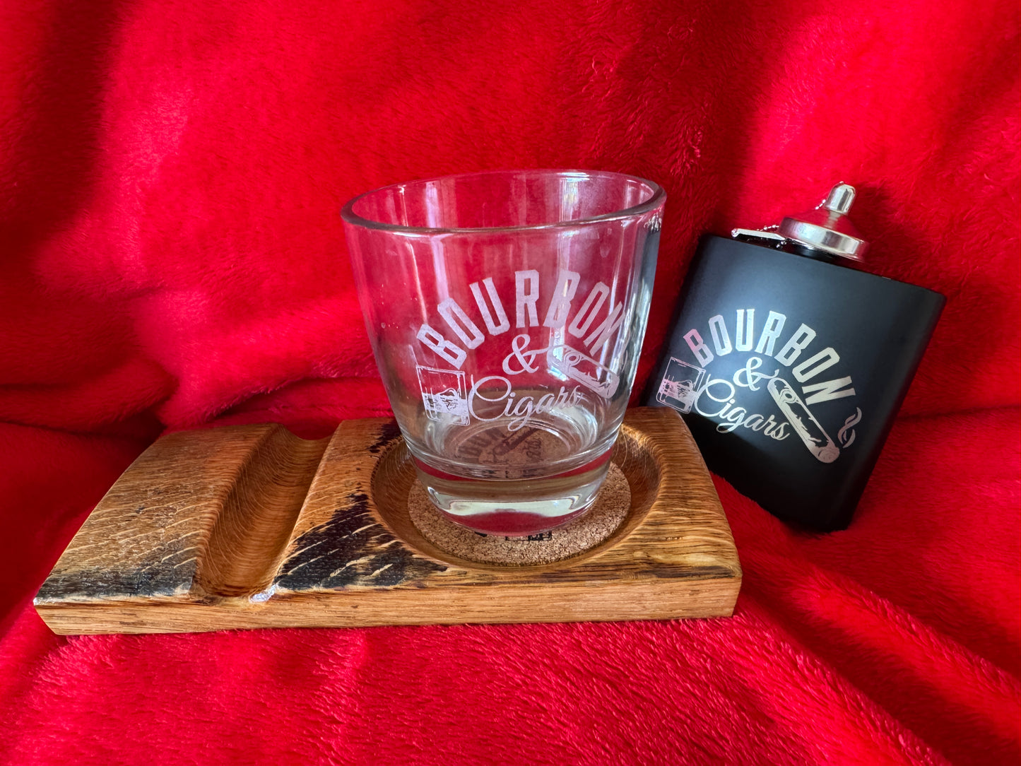 Glass tumbler and black flask with 'Bourbon & Cigars' text on a wooden coaster. Flask sold separately.